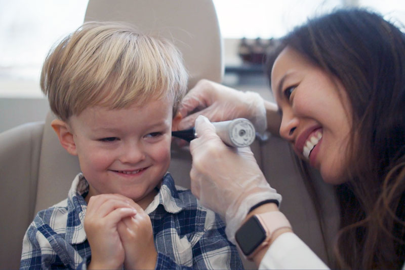 Female ENT physician using an otoscope to examine the inner ear of a smiling young boy