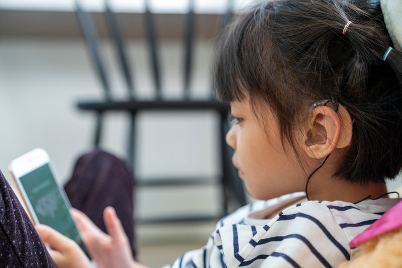Young girl views a tablet while wearing hearing aids
