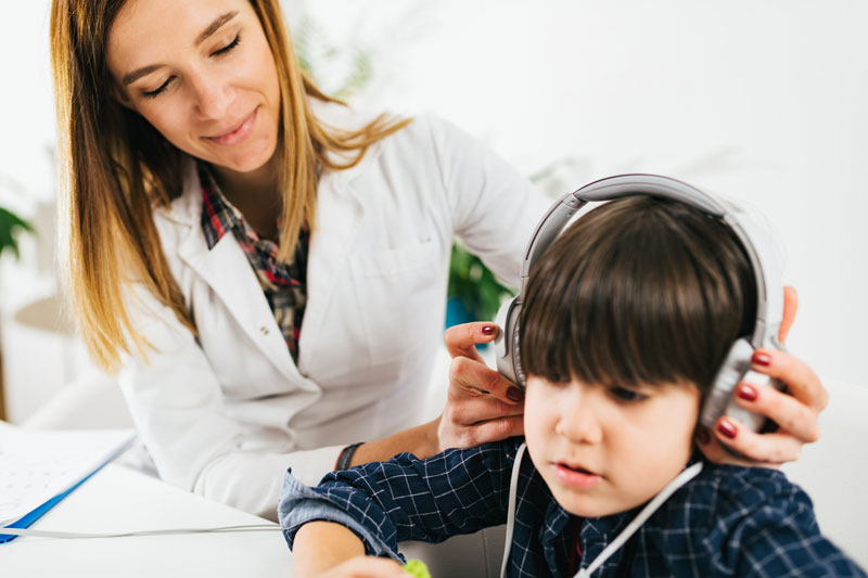 Female audiologist places headphones on young boy to test hearing