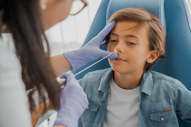 Woman physician uses scope to view nasal passages of young boy patient.