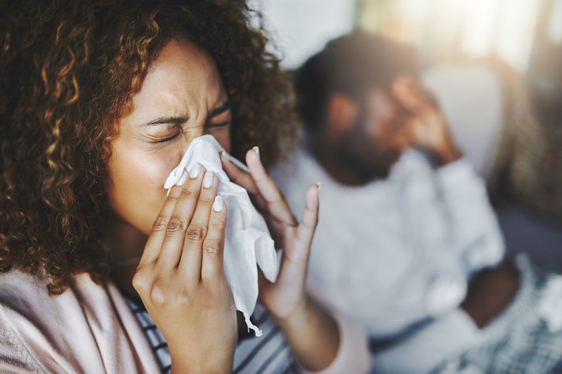 Woman winces as she sneezes into a kleenex