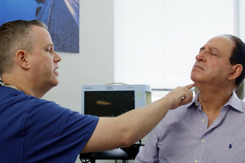 Doctor pointing to something on the neck of an older male patient