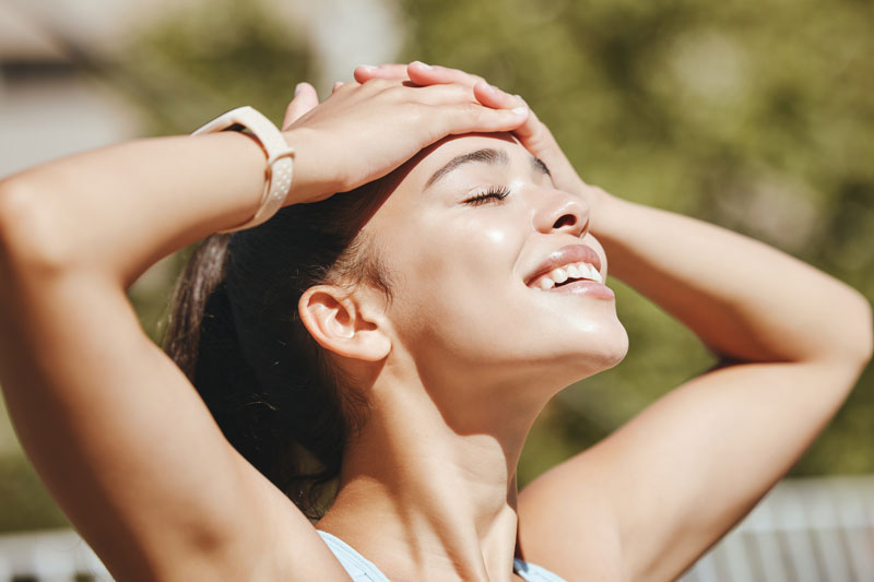 Woman outdoors enjoying weather with hands on her forehead