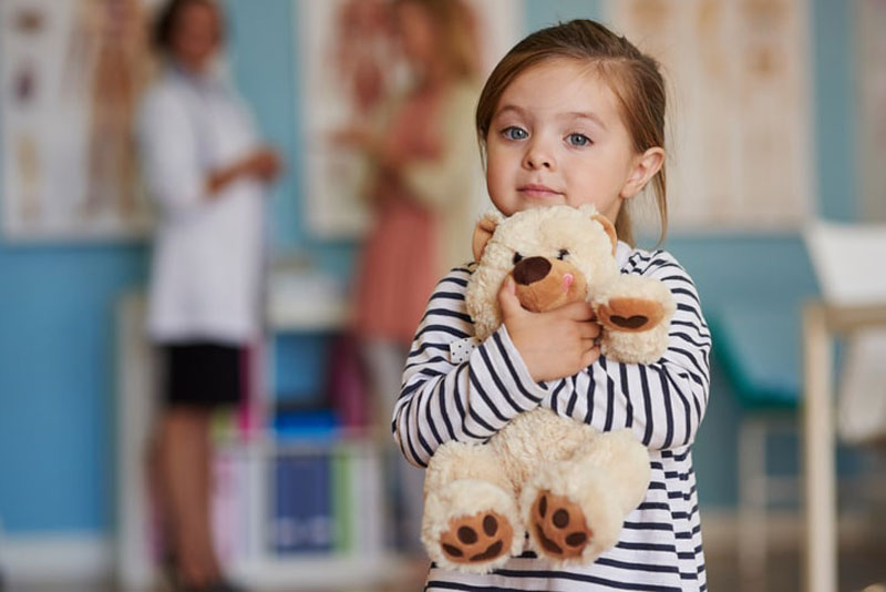 Young girl holding a teddy bear over background ENT doctor consultation