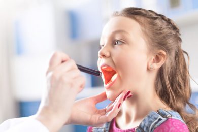 Young girl opens mouth wide while physician examines with light