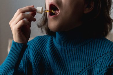 Woman in blue sweater administering drops under her tongue at home.