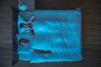 Middle aged man sleeps with his mouth open in bed while woman can’t sleep
